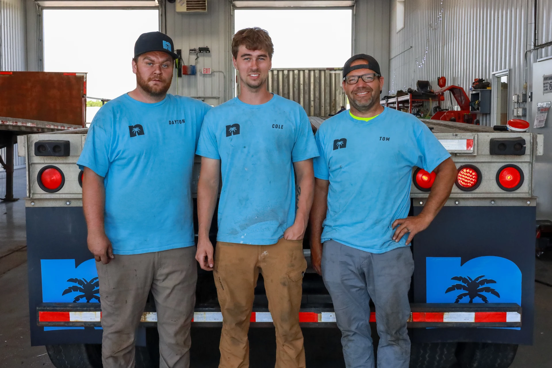 Three members of the Newport shop team standing together in front of a trailer